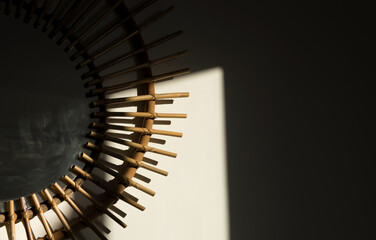 sunset sunbeam entering through the window reflected on the dining room wall and decorative mirror with a frame made of pieces of cane in a warm color
