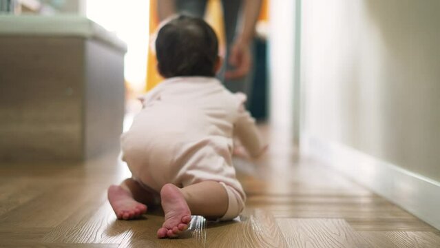 Happy and curious child explores his house by crawling on parquet floor.Father cheers his child up by clapping his hands.Baby crawls across floor towards his parent.Baby learn to move on floor at home