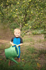 Toddler boy watering garden with watering can. Summer development of children outdoor
