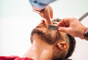 Fototapeta premium Crop barber cutting beard of client with razor
