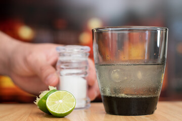 First plane of glass with margarita drink and a hand taking the salt container to prepare the cocktail in bar