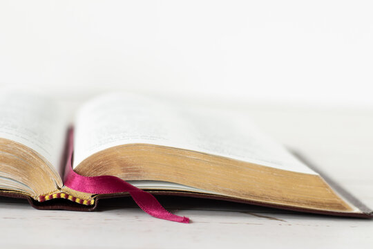 Closeup of open holy bible book with gold pages isolated on wooden table with white background. Copy space. Christian Scripture Study, biblical concept.