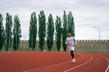 Fototapeta premium Motivated determined young male athlete running on red race track while training at sports stadium in city 