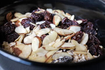Close-up view of dry cereal in a black ceramic bowl. The bowl contains, oatmeal, raisins, and sliced almonds.