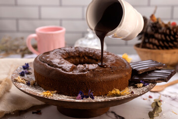 round chocolate cake with chocolate bar and covered in liquid chocolate and decorated with dried flowers and portion of cake served on a plate