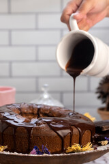 round chocolate cake with chocolate bar and covered in liquid chocolate and decorated with dried flowers and portion of cake served on a plate