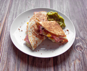 A plate of food with a quesadilla and guacamole on it.