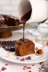 round chocolate cake with chocolate bar and covered in liquid chocolate and decorated with dried flowers and portion of cake served on a plate