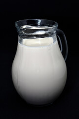 Glass milkman on a black background. A jug of milk. Milk in a vessel.