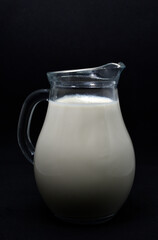 Glass milkman on a black background. A jug of milk. Milk in a vessel.