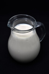 Glass milkman on a black background. A jug of milk. Milk in a vessel.