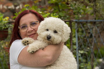 A middle-aged woman holds her curly bison in her arms. A woman with red hair and glasses holds a Bison in her hands.