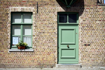 Kunstvoll restaurierte Fassade aus Backstein mit schönem Fenster und Tür in Grün als Teil des Unesco Weltkulturerbe bei Sonnenschein in den Gassen der Altstadt von Brügge in Westflandern in Belgien