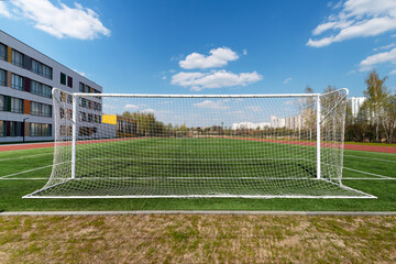Football goal on a school soccer field with artificial grass against a blue sky