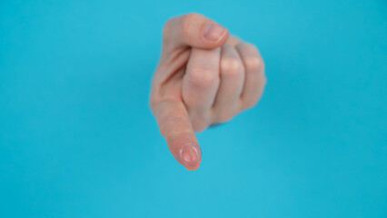 A woman's hand sticks out through a blue paper background and holds a contact lens.