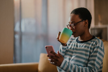 African american woman drinking coffee and using a smartphone at home