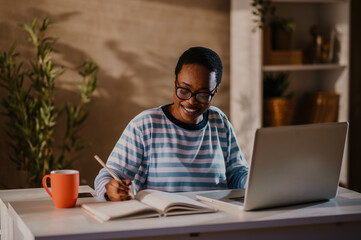 Smiling african american woman a laptop and taking notes while working in a home office