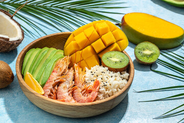 tropical bowl with avocado, prawns, rice, mango, kiwi and coconut, tropical food on the sea beach...