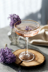 Pink cocktail in vintage glass with flower garnish on raw wood. Iced cold summer drink. Organic natural cocktail, lilac lemonade.  