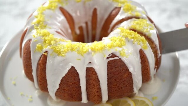 Step by step. Slicing lemon bundt cake decorated with lemon zest on a cake stand.