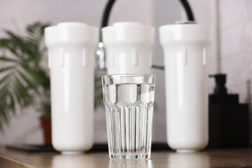 Glass of clean drinkable water and set of filter cartridges on wooden table top in a kitchen,...