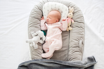 Peacefully sleeping Caucasian newborn baby girl in a baby nest. Baby in a pink bodysuit