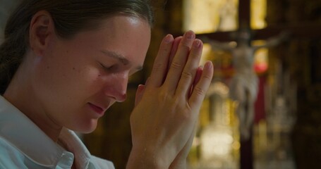 Adult girl bowed her head in thanksgiving prayer to God in church. Young woman folded hands in prayer to Christ the Redeemer.
