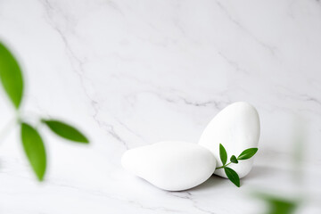 White stone product display platform with green leaves in defocus. White podium on marble background. Podium, stage pedestal or platform. Trendy natural mockup template. Free space.