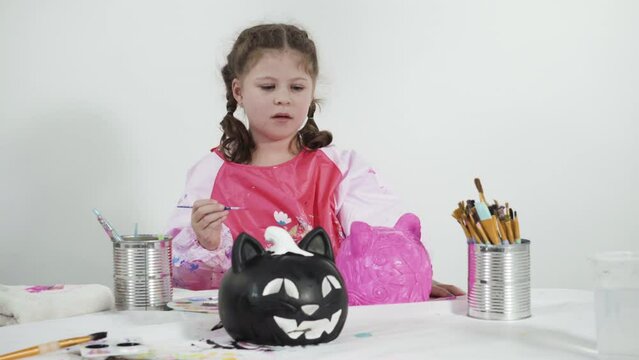 Little girl painting craft pumpkin with acrylic paint for Halloween.