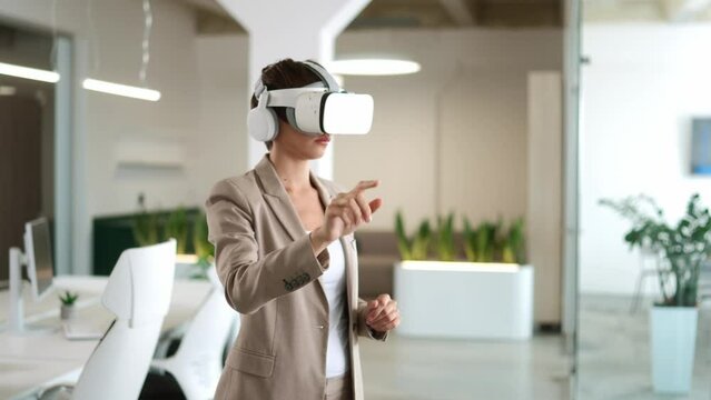 Caucasian businesswoman with elegant suit using innovation virtual reality headset in workplace. Successful female manager previewing financial holograms or animations. Working in developing business.