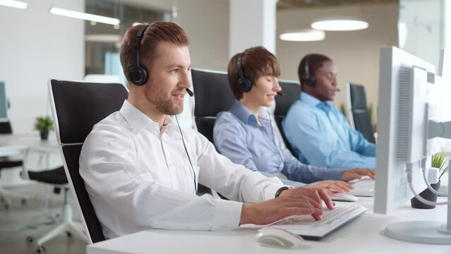 Group of multiethnic operators with headset sitting at desk. Focused answering incoming calls from customers. Working on computers and typing texts on keyboards. Concept of business service.
