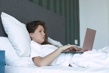 young woman lies and use laptop in bed in the morning. concept online learning, work, shopping