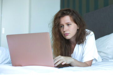 young woman lies and use laptop in bed in the morning. concept online learning, work, shopping