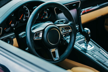 Luxury sports car interior. Steering wheel, shift lever and dashboard. bright leather interior with...
