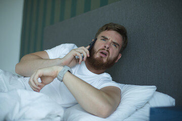 Young sleepy awaken man is just wake up with phone call, looking at his watches checking time and hurry up and yawn. Guy overslept job 