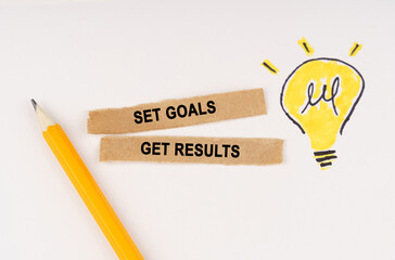On a white surface, a luminous light bulb and pieces of paper with the inscription - Set Goals Get...