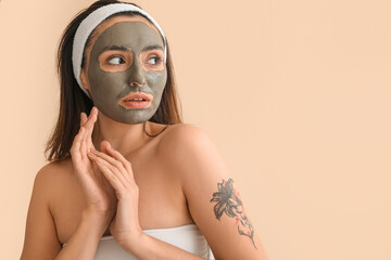 Young woman with applied clay mask on beige background, closeup