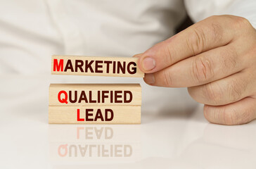 In the hands of a person and on a reflective surface are wooden blocks with the inscription - marketing qualified lead