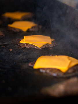 cooking burgers with cheddar cheese on a griddle in fast food restaurant