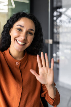 Vertical Shot, Young Beautiful Hispanic Business Woman With Curly Hair Talking On Video Call, Waving At Smartphone Camera, Using Remote Communication App.