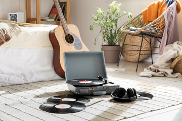 Record player with vinyl disks and guitar in interior of bedroom