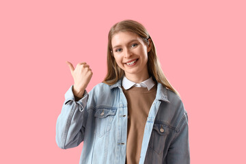 Young woman pointing at something on pink background