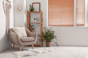 Cozy grey armchair, houseplant, stylish macrame and shelving unit in light room