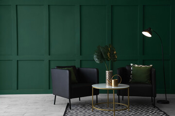Black modern armchairs with cushions, table and lamp near green wall