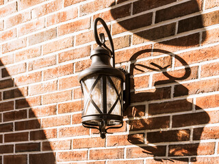 Vintage carriage lamp on a rustic brick wall in strong sunlight with strong shadows