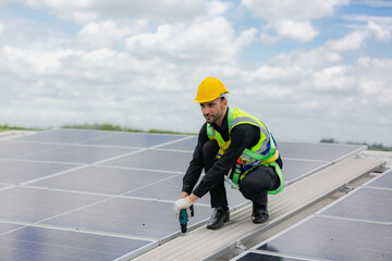 Handsome young male engineer wearing safety vest and jacket with gloves and tools along with hard hat helmet standing on solar panel while checking and looking at its maintenance