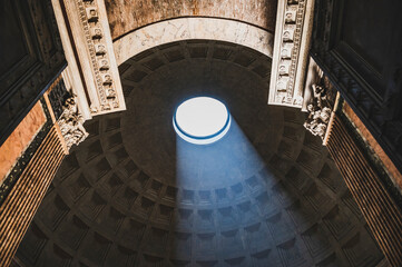 Wnętrze Panteonu w Rzymie z widokiem na imponujący sufit z otworem oculus, przez który wpada światło słoneczne. Ten unikalny widok ukazuje majestatyczną konstrukcję i niesamowite efekty świetlne. - obrazy, fototapety, plakaty