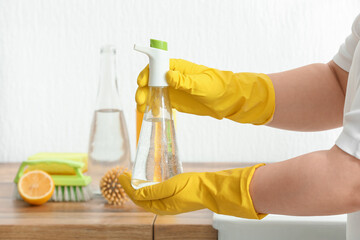 Woman in rubber gloves with bottle of vinegar in kitchen