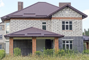 one white private brick house with a brown tiled roof in green grass and vegetation on a rural street