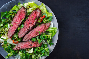 Traditional barbecue bavette beef steak slices with lambs salad and iceberg lettuce served as top view on a design plate with copy space right